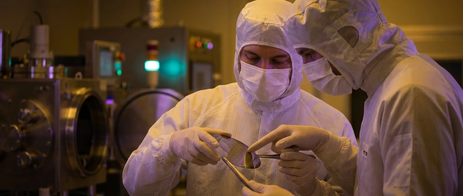 Two engineers in cleanroom suits inspecting a wafer